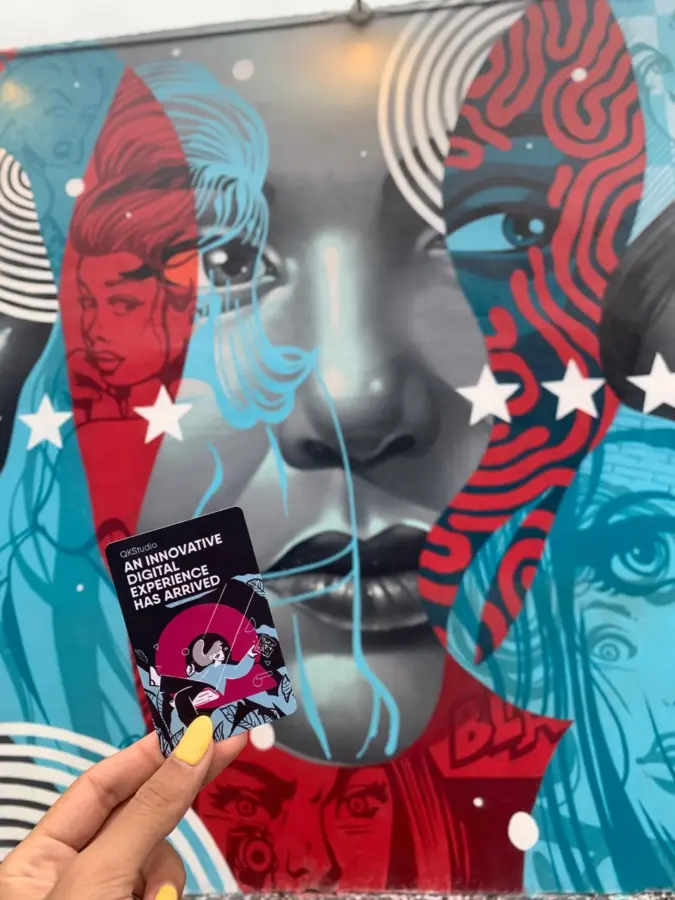 QKStudio card held up in front of a mural in Wynwood, Miami